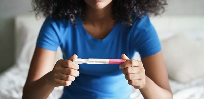 Une femme assise en tailleur sur son lit regardant le résultat de son test de grossesse urinaire.